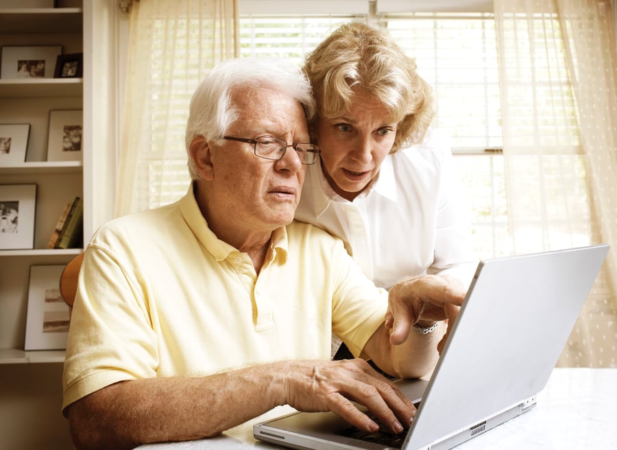 older couple practicing social distancing by using their computer to research financial advisors